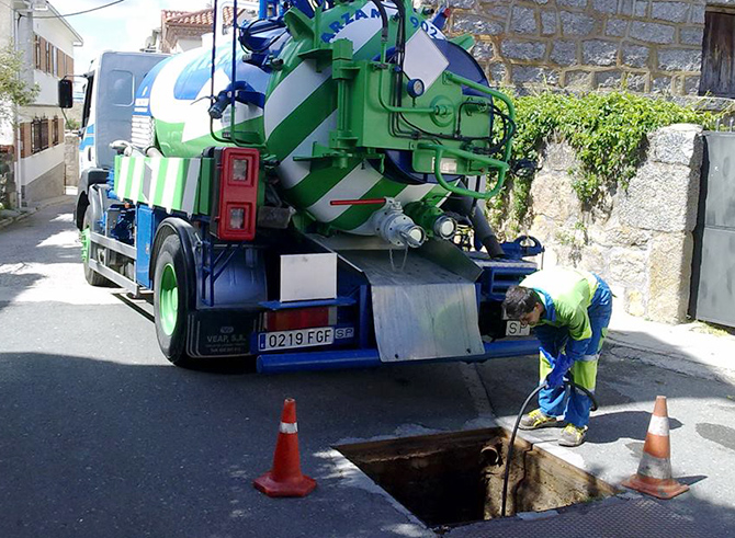 Operario de Arzam realizando servicio de desatasco de alcantarillado con camión cuba en una calle residencial, mantenimiento profesional de redes de saneamiento.