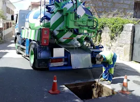 Operario de Arzam realizando servicio de desatasco de alcantarillado con camión cuba en una calle residencial, mantenimiento profesional de redes de saneamiento.