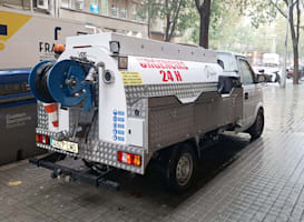 Camión de vacío con logotipo de Tub-Net y texto \DESATASCOS 24 H\ estacionado en una calle mojada, con carrete de manguera y equipo visible en la parte trasera