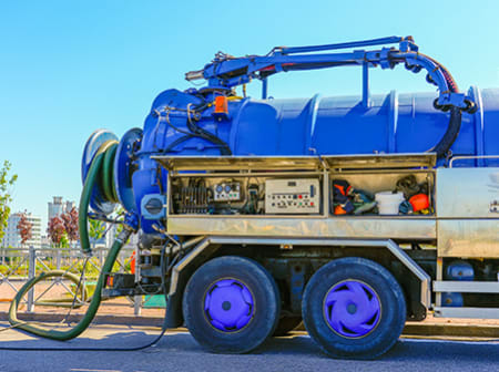 Camión de vacío azul estacionado en la carretera, con panel lateral abierto mostrando controles y herramientas.